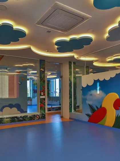 A room with a parrot-themed bookshelf and a sky-like ceiling with backlit clouds. The use of mirrors and glass walls creates a sense of openness and connection between different learning spaces.