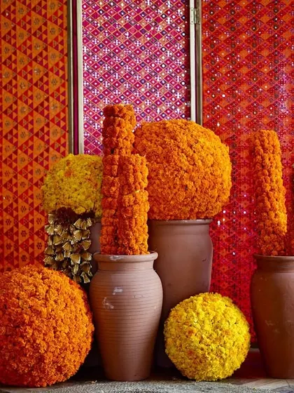 A decorative corner showcasing the theme's core elements. Terracotta pots are filled with bright orange and yellow marigold balls, set against a backdrop of colorful, patterned panels.