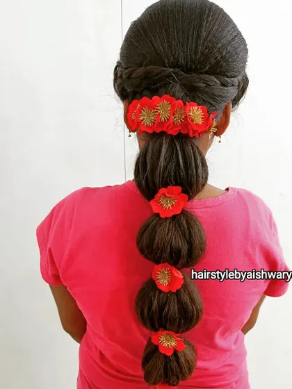 A fun and youthful bubble braid. Each section is accentuated with a bright red floral accessory, creating a playful yet traditional hairstyle.