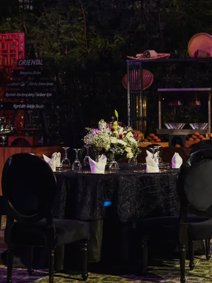 An elegant black-on-black table setting for an outdoor dinner. The setup includes an oriental food station in the background, showcasing the culinary experience.