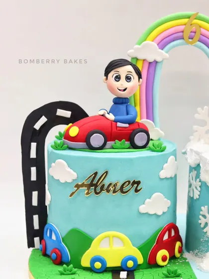 A full view of the car-themed side of the twin's cake. This highlights the fondant road, clouds, and colorful cars that create a playful landscape for the main figurine.