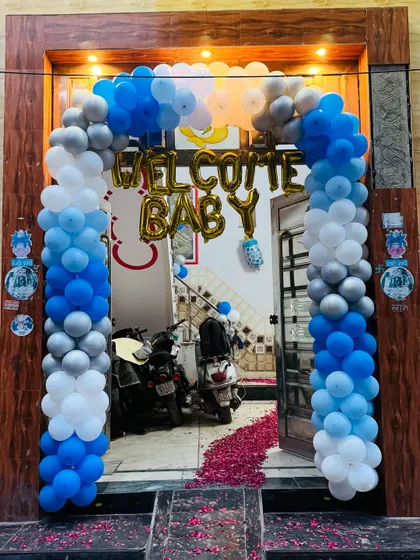 A grand entrance for a 'Welcome Baby' party with a full balloon arch in shades of blue, white, and silver, and a floor covered in rose petals.