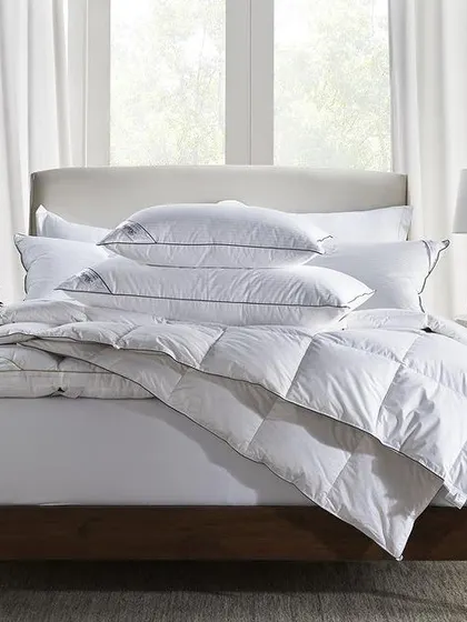 A clean, crisp shot of a fully dressed bed featuring a feather-down comforter and pillows. This image clearly showcases the entire bedding set in a bright, minimalist environment.