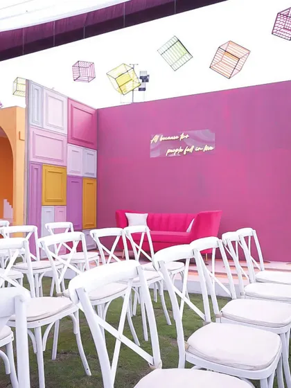 A vibrant seating area with a magenta wall, a neon quote, and colorful geometric cubes hanging from the ceiling.