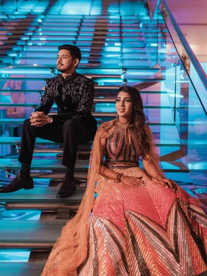 A stylish portrait of a couple seated on a modern, illuminated staircase, showcasing their stunning outfits and the contemporary decor of the event.