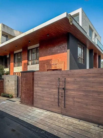 The entrance gate and boundary wall of the Hennur residence, featuring a mix of exposed brick and solid wood for a robust and welcoming statement.