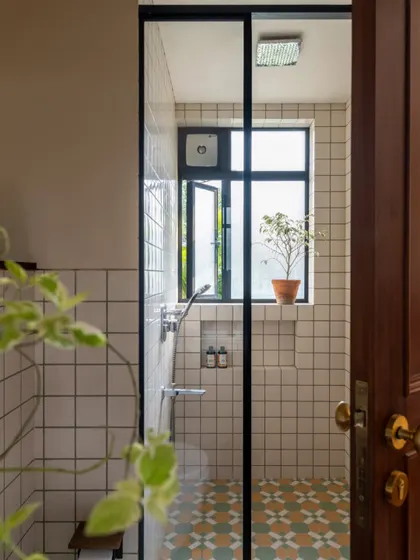 A light-filled bathroom in Calcutta, where simple white tiles are paired with a colorful patterned floor. The design is clean and fresh, with a large window in the shower that connects the space to the outdoors.