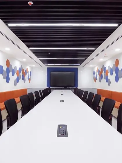 A conference room featuring bench seating and a large central table, perfect for collaborative workshops. The geometric acoustic panels on the wall are both a design feature and a functional element for sound absorption.