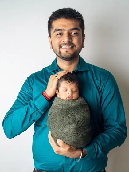 A proud father holds his swaddled newborn, smiling at the camera. This is a classic first portrait that captures the joy and pride of being a new dad.