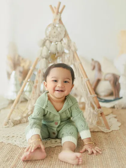 Cuteness overload. This happy one-year-old is all smiles during his birthday photoshoot, sitting in front of a fun teepee setup in the studio.