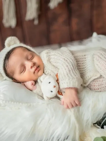 A slightly different angle of the miniature bed scene, showing the baby cuddling a small teddy bear.