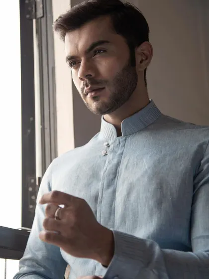 A light blue linen shirt with a mandarin collar and unique button details. This piece blends comfort and elegance, perfect for summer.