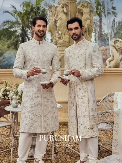 In the heart of elegance, two gentlemen find themselves amidst timeless grandeur. Their coordinated ivory sherwanis are designed for savoring the art of a quiet moment.