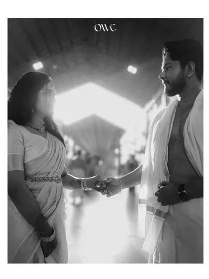 A stunning black and white silhouette of a couple holding hands inside a temple corridor, with light streaming in.