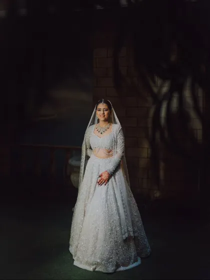 A full-length portrait of a bride in a stunning white lehenga, captured with dramatic lighting that makes her stand out.