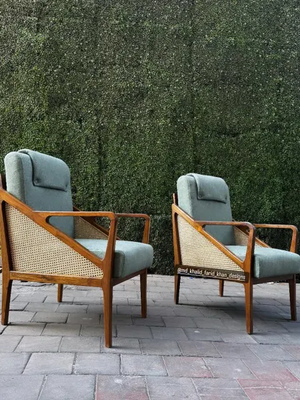 A pair of high-back lounge chairs featuring an elegant design with cane side panels and a comfortable, adjustable headrest cushion.