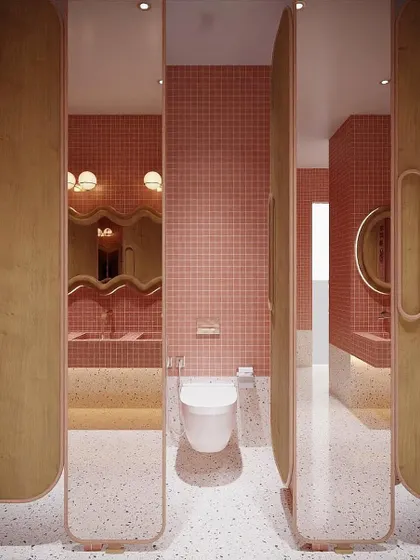 The entrance to the washroom stalls, featuring full-height mirrored doors with custom wood handles. The combination of pink mosaic tiles and terrazzo flooring creates a fun and luxurious feel.