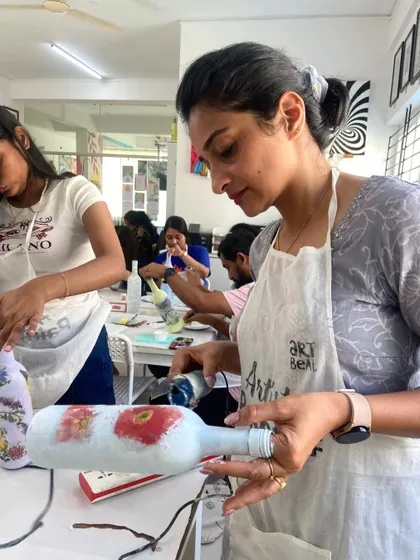 A participant works on her decoupage bottle, carefully placing the paper cutouts. It's a craft that combines painting, cutting, and pasting.