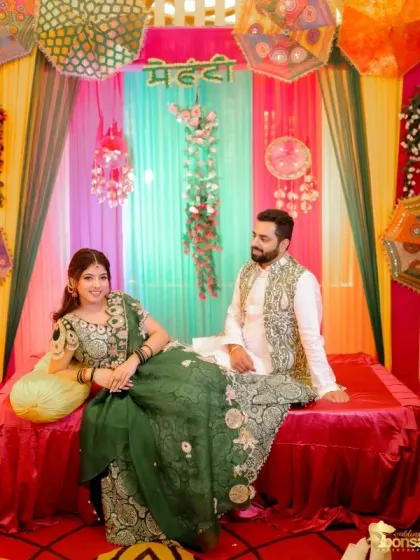 A classic portrait of the couple at their Mehndi ceremony, seated against a colorful backdrop.