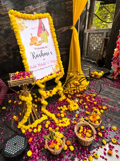 A detailed look at an entrance setup for a Haldi Mahotsav. I used a custom welcome sign, flower petals scattered on the floor, and small decorative props like a bicycle to create an inviting atmosphere.