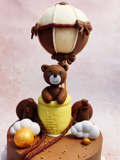 We take to the skies with this charming teddy bear hot air balloon cake. This "Oh Baby!" themed cake features adorable teddy bears on a chocolate-frosted tier, with one bear soaring high in a meticulously crafted hot air balloon.