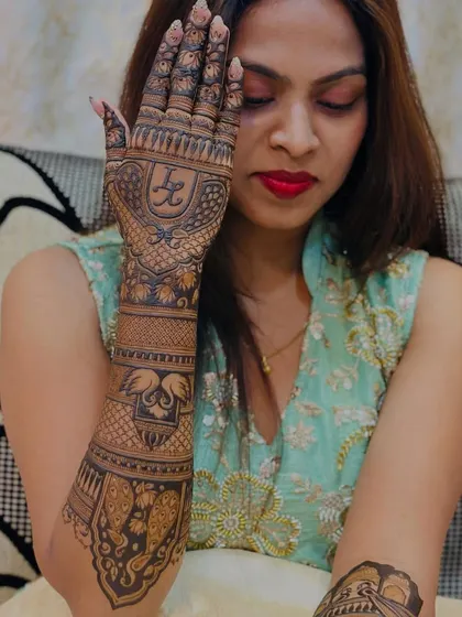 A bride showcasing one full arm of her mehendi, which features her initials, swans, and elephants.
