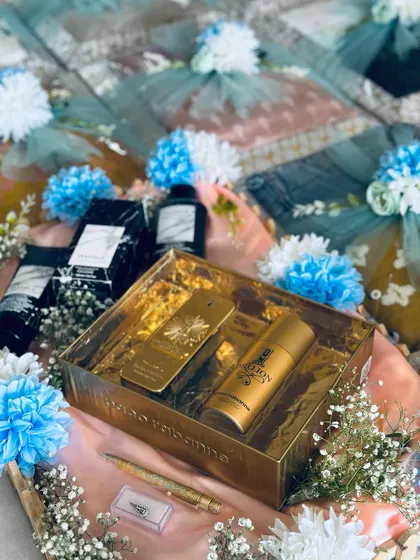 A luxury gift set for the groom, part of an engagement trousseau. This golden box contains premium perfume and deodorant, surrounded by delicate flowers.