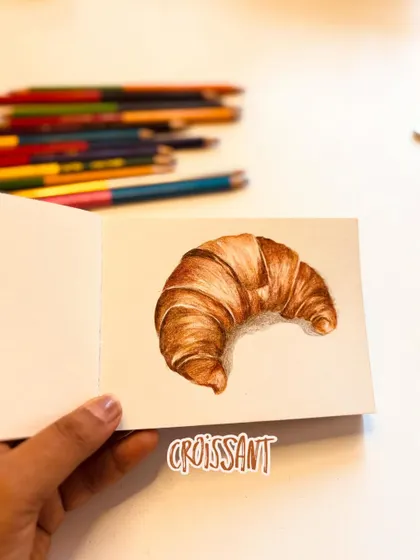 The croissant drawing in my sketchbook, with the color pencils I used nearby.