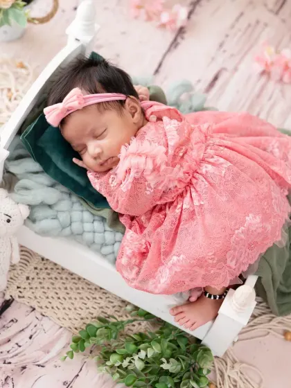 A sleeping newborn princess in a frilly pink lace dress, resting on a tiny white bed.