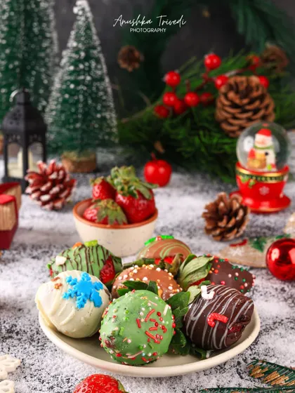 A wider view of the festive chocolate-dipped strawberries, surrounded by miniature trees, a snow globe, and other Christmas props.
