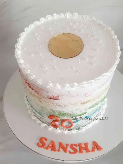 A dairy-free rainbow cake for a 30th birthday. This cake has a subtle rainbow watercolor effect on the outside and a clean, minimalist finish on top.