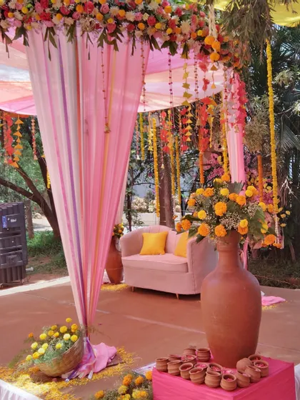 A lovely outdoor stage setup with pink drapes and earthen pots filled with marigolds.