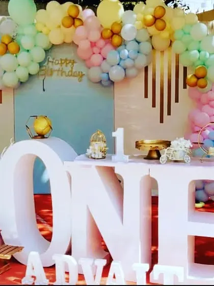 A stunning first birthday setup featuring a large "ONE" table as the centerpiece. The pastel rainbow balloon arch and clean white props give it a modern and stylish feel.