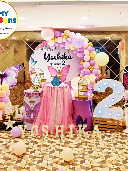 A breathtaking butterfly theme for a second birthday. This setup features a mirrored floor, a central tulle-draped table, large butterfly cutouts, and a pink and purple balloon arch, creating a truly magical atmosphere.