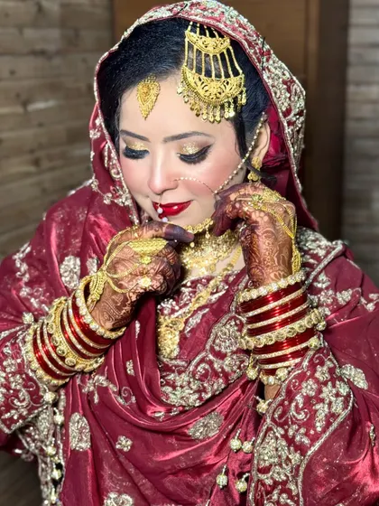 This bride is adjusting her nath, a classic moment on the wedding day. Her HD makeup features a bright red lip and golden glittery eyes, a timeless combination for a Nikkah ceremony.
