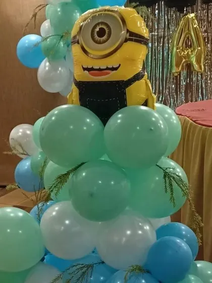 A close-up of a Minion character foil balloon sitting atop a pillar of green and white balloons.