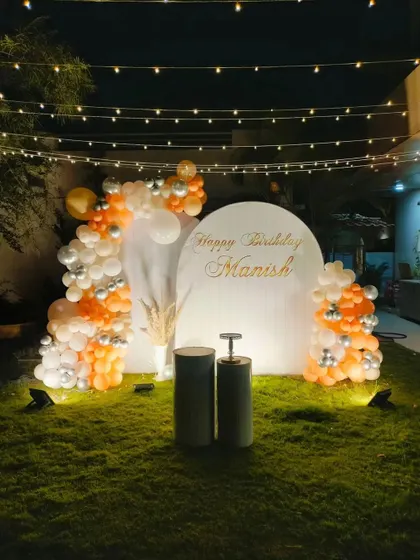 A simple yet elegant birthday backdrop set up on a lawn for an evening celebration, with string lights overhead.