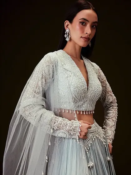 An elegant look in a pastel blue lehenga. The makeup is kept fresh and minimal, with sleek hair pulled back to highlight the delicate lacework of the full-sleeved blouse.