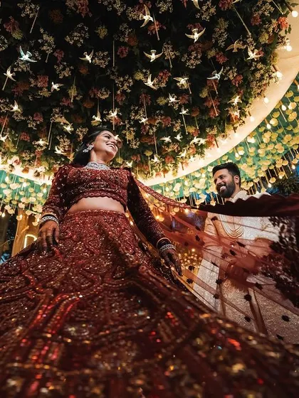 A grand reception portrait. The bride's swirling lehenga and the magnificent floral ceiling create a breathtaking image full of movement, color, and opulence.