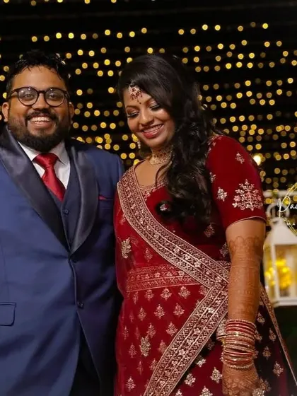 A happy couple shot from a reception. The bride is wearing a rich red velvet lehenga, and her makeup features a soft smokey eye and a warm lip color to match the festive atmosphere.