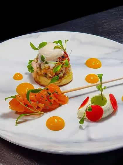 A gourmet appetizer plate featuring salmon skewers and other small bites. The presentation on a marble plate with artistic sauce drops shows our attention to detail.
