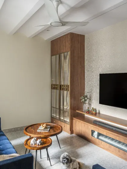 This multifunctional living room unit seamlessly combines an entertainment zone with a discreet puja area, all unified by a soothing palette of warm woods and muted cream tones.