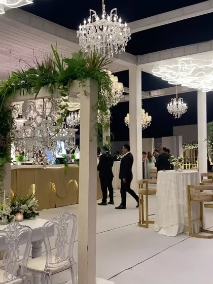 A stylish bar area that is both functional and beautiful. The custom white and gold bar is framed by a greenery-clad arch, with elegant high-top tables providing a chic space for guests to mingle.