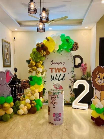 A "Two Wild" themed birthday decoration for a second birthday party at home. This setup includes an arched backdrop, a balloon garland, animal cutouts, and a light-up marquee number '2'.