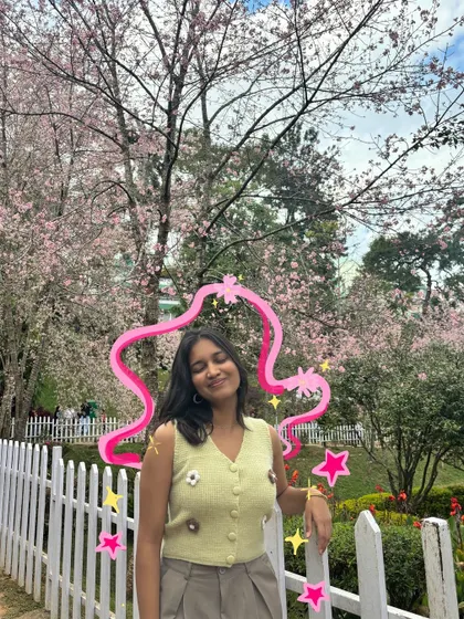 Leaning against a white picket fence surrounded by cherry blossoms, with a cute pink frame doodled around me.