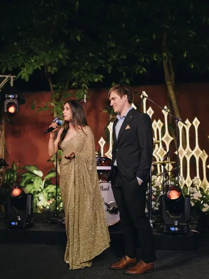 A candid moment of the bride speaking at her cocktail party. The one-shoulder saree is a modern and chic choice for an evening celebration.