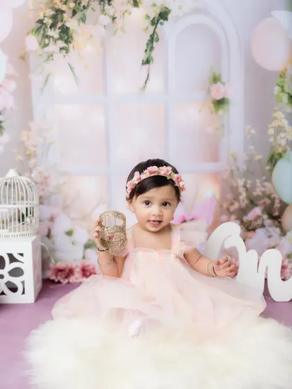 A classic first birthday portrait, complete with a "One" sign and a beautiful, soft backdrop.