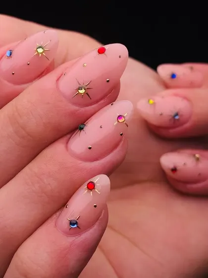 A galaxy of sparkle on your fingertips. This design features a sheer nude base dotted with tiny, colorful starburst gems for a delicate and magical effect.
