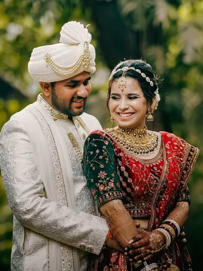 The couple shares a warm embrace, their coordinated red and white outfits looking regal against the natural green background. Their happy expressions tell a story of love and companionship.