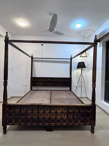 A classic four-poster bed frame made from dark, intricately carved wood. This showcases the quality of our custom furniture even before the room is fully dressed.